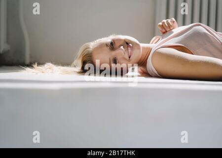 Portrait of smiling blond young woman lying on the floor Stock Photo