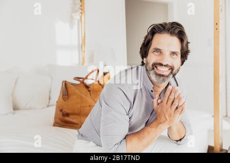 Portrait of happy bearded man sitting on bed Stock Photo