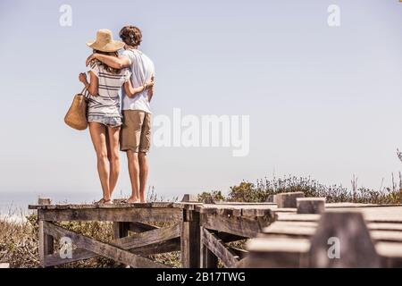 Young couple standing on a boardwalk at the coast looking at view Stock Photo
