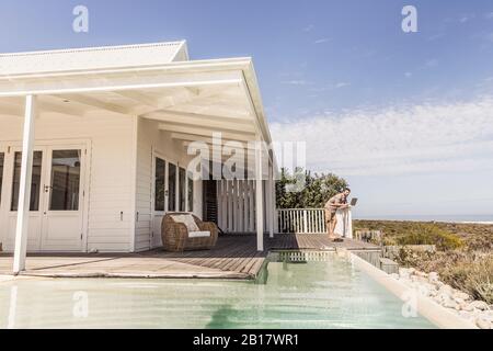 Man working on laptop next to pool at a beach house Stock Photo