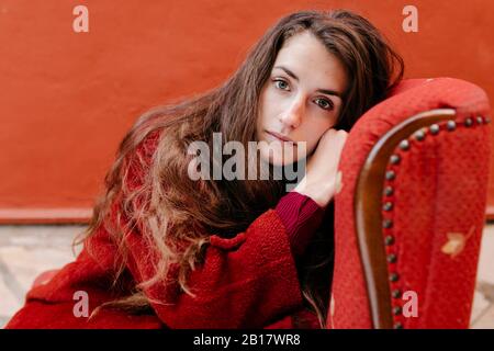 Portrait of young woman dressed in red sitting on lounge chair Stock Photo