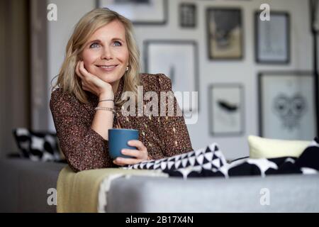 Smiling blond woman relaxing at home sitting on couch Stock Photo