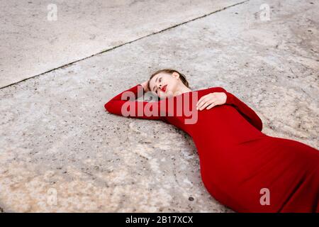 Portrait of young woman wearing red dress lying on ground outdoors Stock Photo