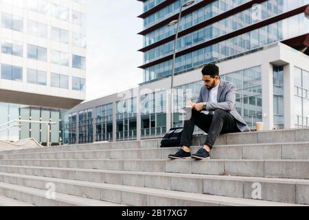 Casual young businessman sitting on stairs in the city taking notes Stock Photo