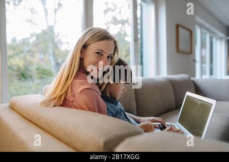 Mother and son sitting on couch, using laptop Stock Photo
