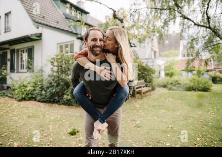 Woman kissing man, carrying her piggyback in garden Stock Photo