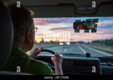 Senior man driving a car on a highway at sunset Stock Photo