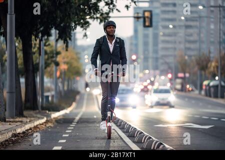 Portrait of businessman riding push scooter on bicycle lane in the evening Stock Photo