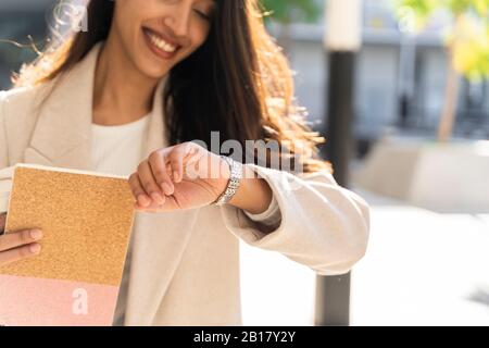 Smiling young woman with book checking the time Stock Photo