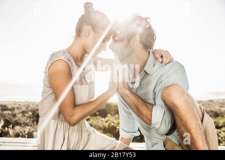 Affectionate young couple hugging on terrace at the coast at sunset Stock Photo