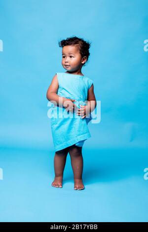 Portrait of barefoot little girl wearing light blue dress standing against blue background Stock Photo