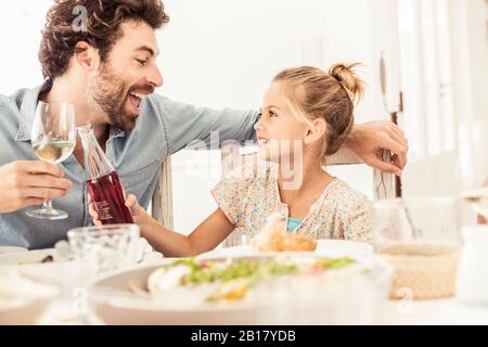 Father and daughter sitting at dining table toasting Stock Photo