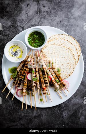 Skewers of meat on plate with yogurt and parsley sauce with flat bread and vegetables Stock Photo