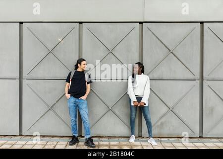Young man smiling at woman at a grey wall Stock Photo