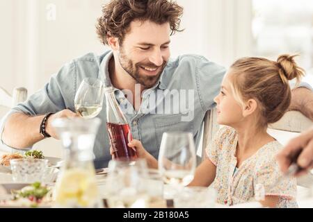 Father and daughter sitting at dining table toasting Stock Photo