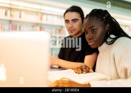 Two students with laptop and book learning in a library Stock Photo