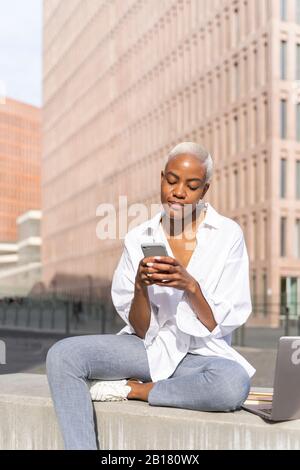 Businesswoman sitting in the city, using smartphone Stock Photo
