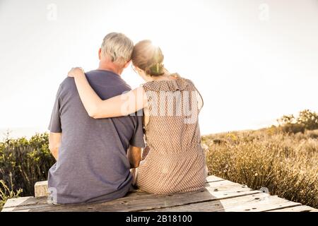 Rear view of couple sitting on boardwalk at sunset looking at view Stock Photo