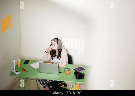 Young woman sitting at desk in office thinking Stock Photo