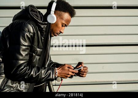 Man with headphones, smartphone and e-scooter outdoors Stock Photo