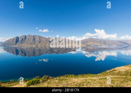 New Zealand, Queenstown-Lakes District, Wanaka, Hills and blue summer sky reflecting in Lake Hawea Stock Photo