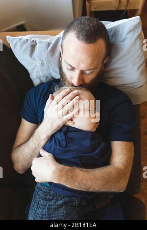 Father kissing his sleeping son on the sofa Stock Photo