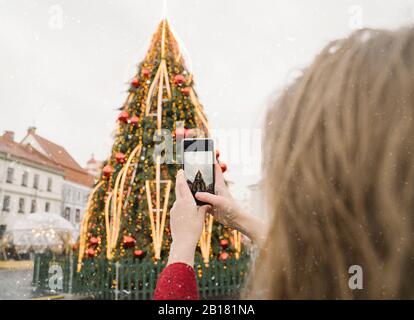 Crop view of woman taking photo of Christmas tree with smartphone on a snowy day Stock Photo