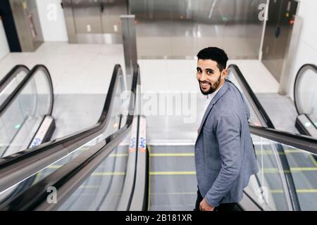 Portrait of smiling young businessman on escalator turning round Stock Photo