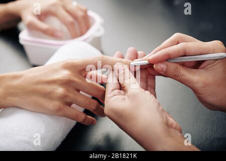 Close-up image of nail master pushing cuticle with metal manicure tool Stock Photo