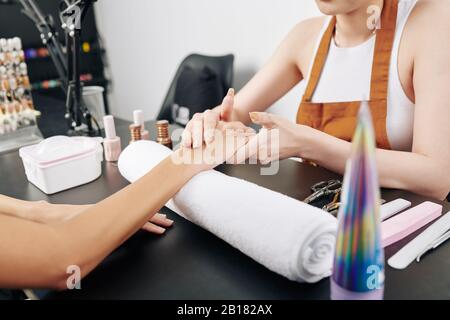 Manicurist applying moisturizing lotion on hand of female client after doing manicure Stock Photo