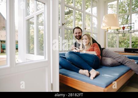 Happy couple relaxing on couch, using smartphone Stock Photo