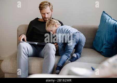 Father and son looking at book on couch at home Stock Photo