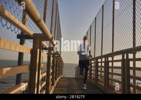 Young woman running on a footbridge at the sea Stock Photo