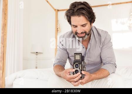 Bearded man sitting on bed with old-fashioned camera Stock Photo