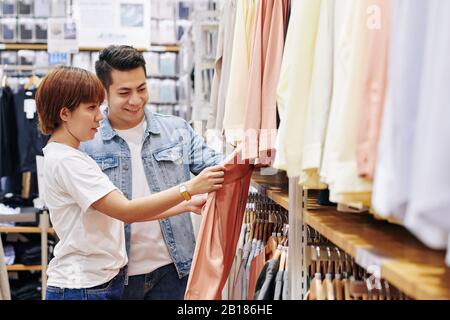 Happy young Asian couple in love shopping for clothes together Stock Photo