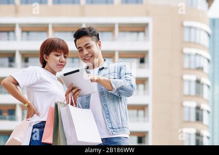 Happy young Vietnamese couple using application on tablet computer when shopping online Stock Photo