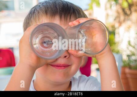 Young traveler with binoculars from two glasses. Fun, positive emotions. Child having fun outdoor. Boy looks through two glasses. Smile on boy's face. Facial expression. Funny family story Stock Photo