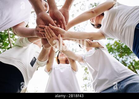 Team of student volunteers stacking hands to show support and unity before starting cleaning college campus Stock Photo