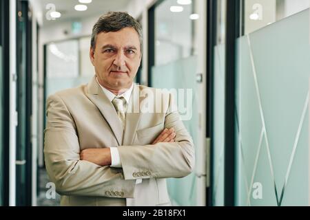 Portrait of confident serious middle-aged entrepreneur standing with arms folded Stock Photo
