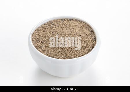 Black peppercorns ground (Piper nigrum) in a white bowl on white background. Used as a spice in cuisines all over the world. Stock Photo