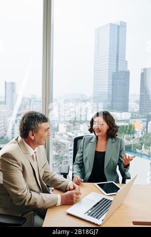 Positive pretty mature businesswoman discussing successful project with colleague Stock Photo