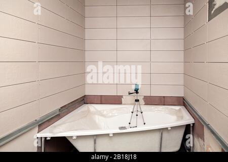 Bathroom interior with white rectangular ceramic tiles on walls, electronic level in bath, repair, reconstruction, even rows of new tile Stock Photo