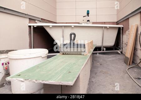 Bathroom interior, putty knife, dirty bucket, ceramic tiles, electronic level in bath, reconstruction, bottom view Stock Photo
