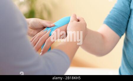 Female physiotherapist applying kinesio tape on patient's arm. Kinesiology, physical therapy, rehabilitation concept. Cropped shot. Stock Photo
