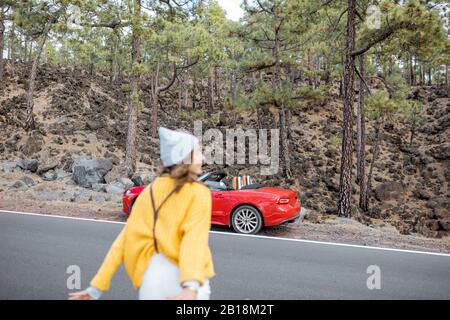 Woman traveling by car in the forest, running on the road, view from the backside. Image focused on the background, woman is out of focus
