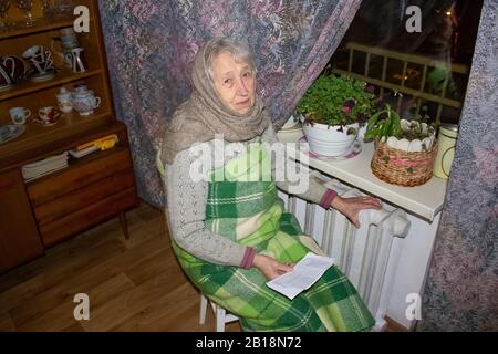 Woman holding cash in front of heating radiator. Payment for heating in winter. Stock Photo