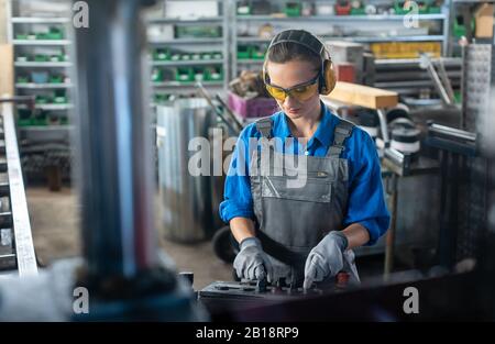 Woman worker operating a machine tool in metal workshop or factory Stock Photo