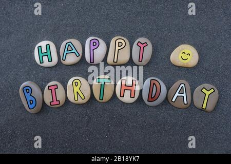 Creative happy birthday with colored letters on sea pebbles over black volcanic sand Stock Photo
