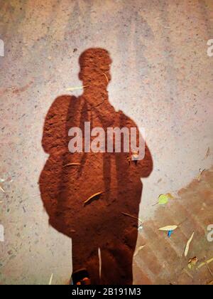 Shadow of a School Boy standing with Bag on City Street. Shadow of a men on street concrete background.Dark shadow on the street of the countryside. S Stock Photo