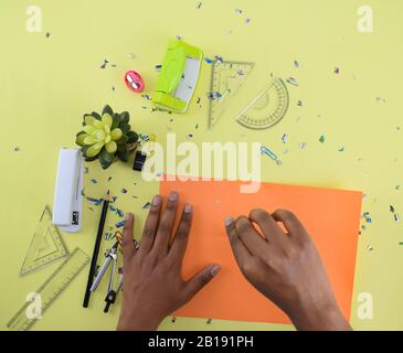 Different study materials scattered on a yellow paper background while a person is drawing on a orange paper with a compass Stock Photo